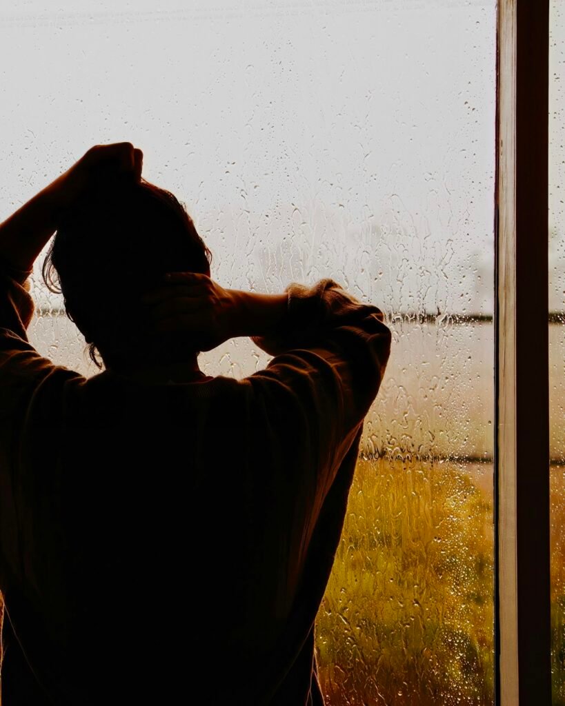 A man standing at a window covered in rain