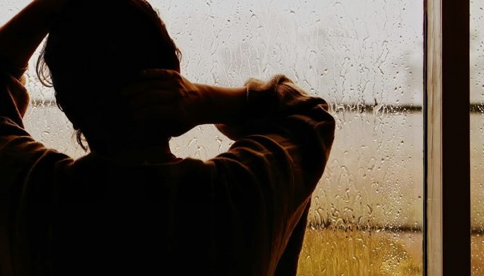 A man standing at a window covered in rain
